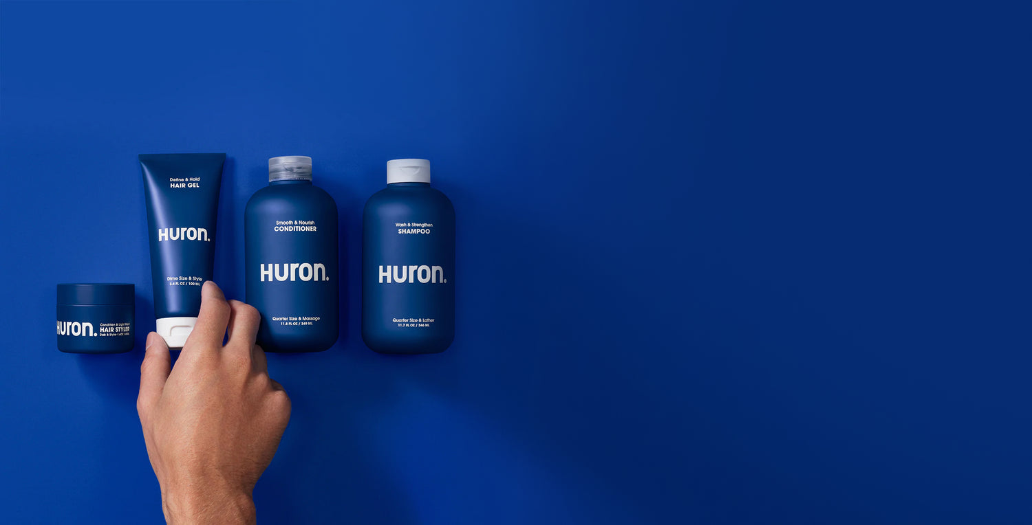 Shampoo, conditioner, hair gel, and hair styler bottles are lined up against a deep blue background. 