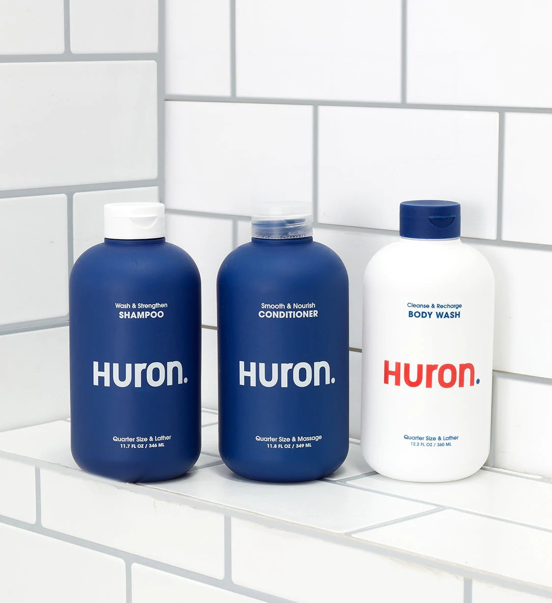 Shampoo, conditioner, and body wash are lined up on a white tiled shower ledge. 